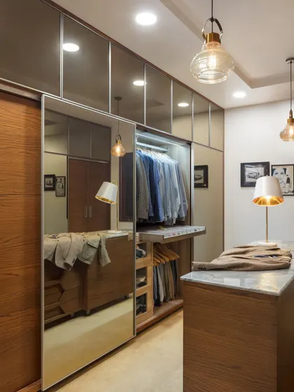 The walk-in closet at Ridge View is positioned along the hallway. Tall, mirrored shutters open into a space rendered in soft brown tones, with a mix of wardrobes and drawers to neatly store the client's collection.