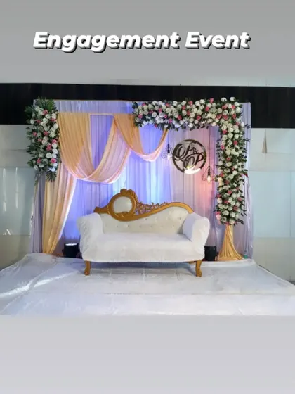 An elegant engagement stage setup with peach and white drapes, a floral arch, and a custom monogram for the couple. The soft lighting and white fur carpet add a touch of luxury.