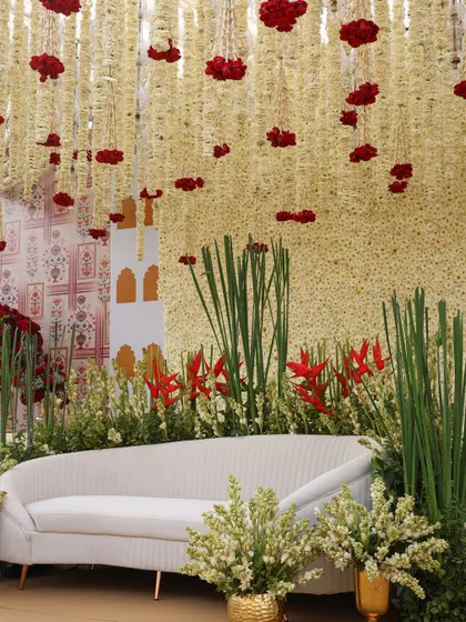 A modern take on traditional decor. This seating area features a backdrop of white flowers with pops of red, under a ceiling of hanging rajnigandha.