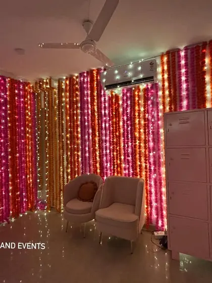 The combination of pink and orange marigold strings with twinkling lights creates a vibrant and celebratory atmosphere for any traditional event.
