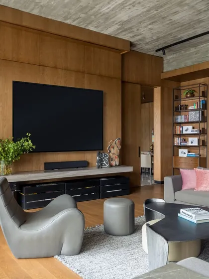 The TV lounge in the K Residence features a comfortable grey leather lounge chair and a sculptural coffee table from our Koko collection. The space is designed for casual relaxation, with a large screen and integrated sound system set against a warm wood-paneled wall.