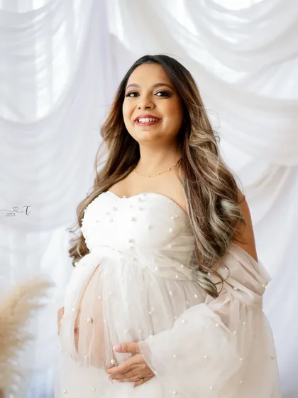A radiant and joyful portrait. The mom-to-be is all smiles in a beautiful white pearl-studded gown, glowing with happiness.