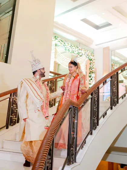 An elegant shot of the Bengali bride and groom on a grand staircase. Their traditional attire and the classic setting create a regal portrait.