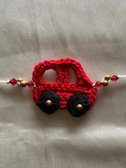A handmade crochet rakhi designed to look like a little red car. This is a fun and unique option for kids during the festival of Raksha Bandhan.