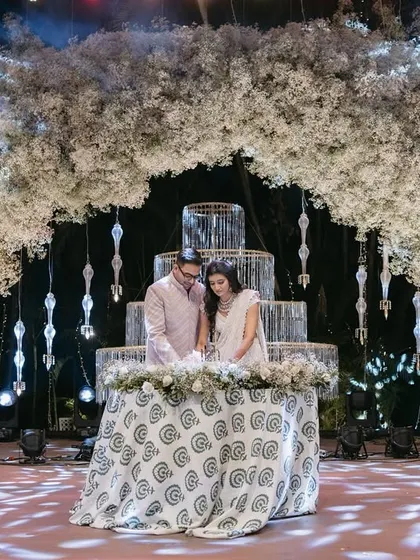 A grand moment for the couple as they cut their cake under a massive arch of white baby's breath, framed by sparkling cold pyro fireworks.