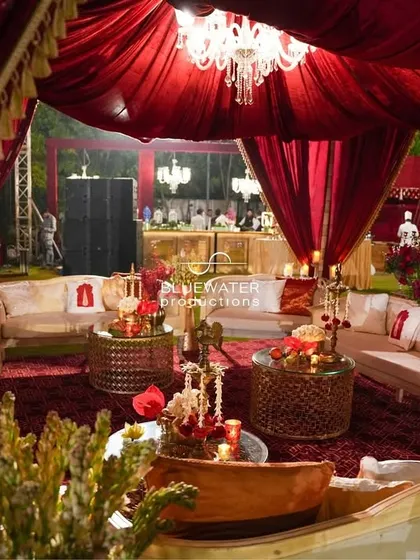 An opulent lounge area set within a tent of royal red drapes, featuring classic furniture, patterned carpets, and the warm glow of chandeliers.