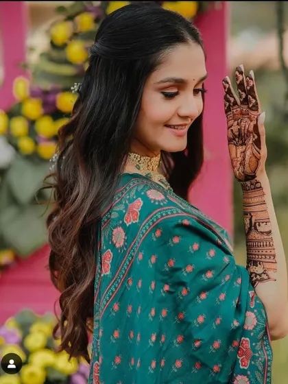 A happy bride showing her story-based mehndi. One hand features a portrait, while the arm shows a detailed scene, making her bridal henna truly one of a kind.