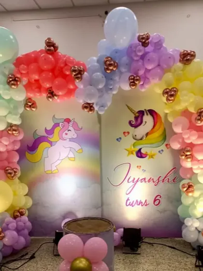A magical unicorn-themed backdrop for a 6th birthday. The decoration includes two arches with pastel rainbow balloons and unicorn illustrations.