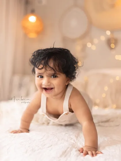 A close-up of a happy, crawling baby with a big smile. The warm, bohemian-style setup with fairy lights adds a cozy and magical feel to this sitter session.