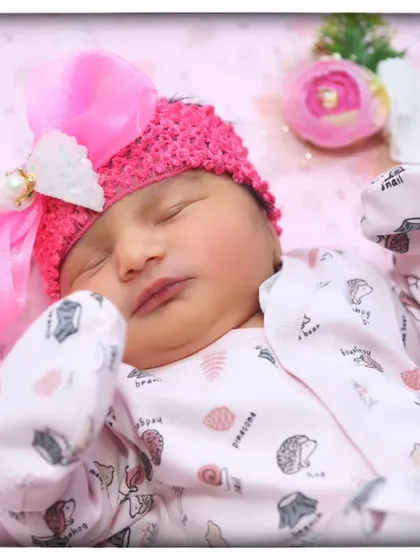 A close-up portrait of a sleeping newborn, showing the delicate details of her face and the soft pink bow in her hair.