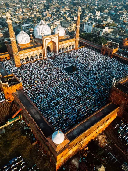 A closer, angled drone shot focusing on the main courtyard of Jama Masjid, filled with worshippers. This view provides a more detailed look at the crowd and the architectural details of the mosque's facade and minarets.