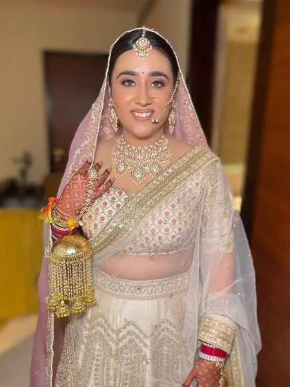 A close-up of the bride in her white and gold lehenga, showcasing her beautiful smile and the intricate jewellery she rented.