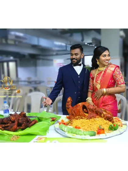 The couple proudly stands by their wedding feast, a testament to the grand celebration.