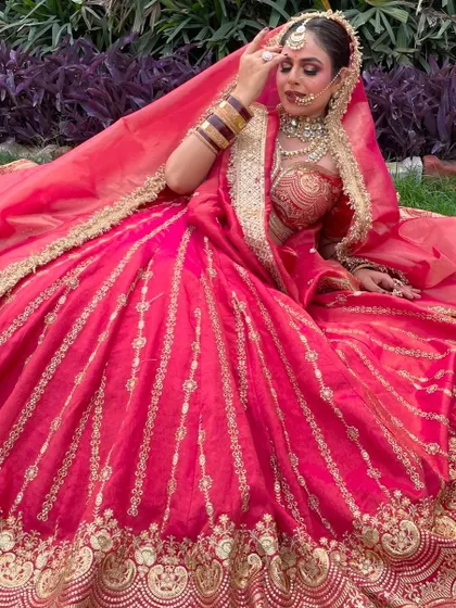 A graceful seated pose in a red lehenga, showing the flow and fall of the fabric and the detailed golden embroidery on the border.