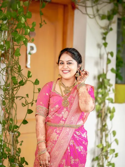 A beautiful portrait of the bride in her pink saree, framed by lush green vines.