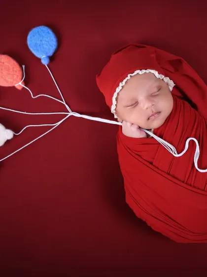 A whimsical newborn photo with the baby holding a string of tiny felt balloons. This creative touch adds a sense of wonder and dreaminess to the portrait.