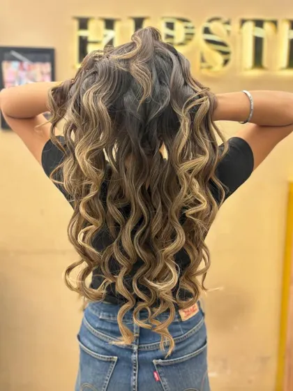A stunning example of balayage on long, curly hair. The color enhances the texture and definition of the curls.