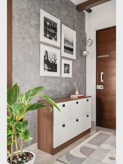 The foyer of the 'Nordic Grey Apartment' features a concrete-textured wall and a dual-toned shoe credenza. The client's own monochrome photography is used as personal and meaningful art.