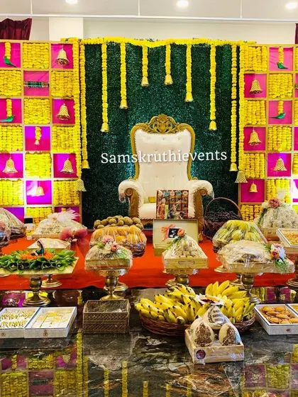 A closer look at the vibrant Seemantha backdrop with yellow flowers and hanging bells. The offerings are beautifully arranged and wrapped, showcasing the attention to detail in my work.
