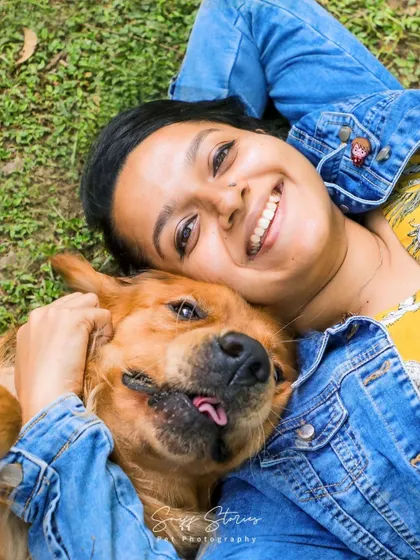 An overhead shot capturing the pure joy and laughter as a woman lies on the grass, cuddling with her goofy Golden Retriever.