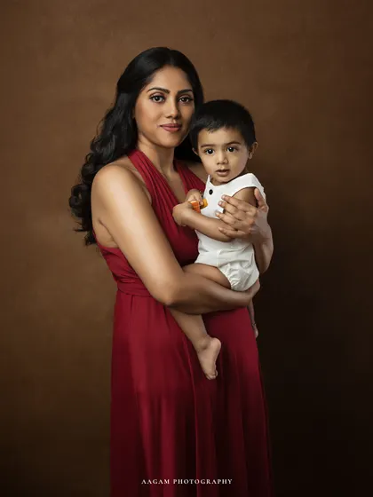 A close-up fine art portrait of a mother holding her child. The warm brown backdrop and her direct gaze create a powerful and soulful image.