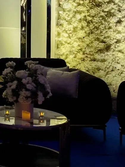 The combination of a modern black sofa, a marble-topped table, and a dense floral wall creates a sophisticated seating area.