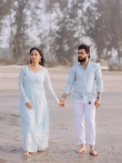 A full-length shot of the couple walking on the beach, capturing their coordinated outfits and the serene coastal environment.