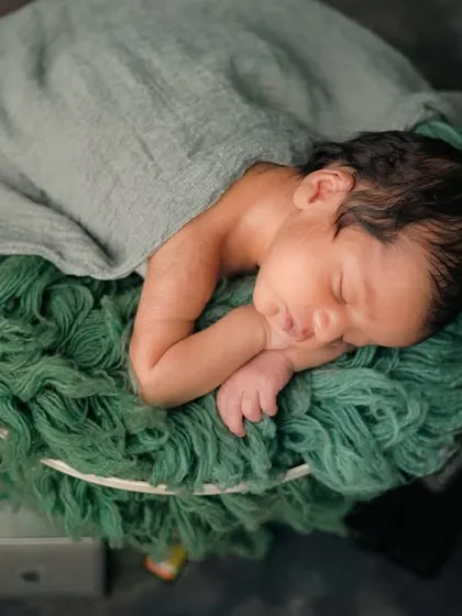 A top-down view of the 'Baby Director' setup, showing the newborn nestled comfortably in the green, textured basket, surrounded by professional camera gear.