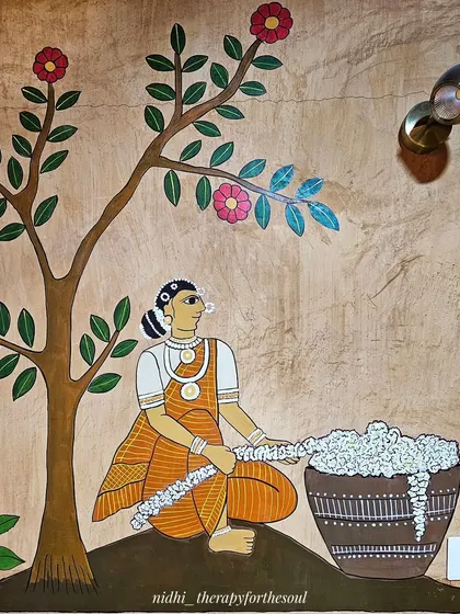 A woman sits under a flowering tree, weaving a garland. The intricate details in her jewelry and the texture of the flowers are hallmarks of the Cheriyal style.