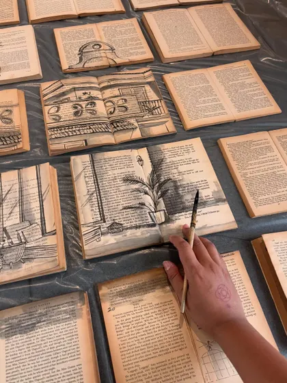 A process shot of 'The Villa between Pages', showing my hand adding details to the architectural sketches on the vintage book pages.