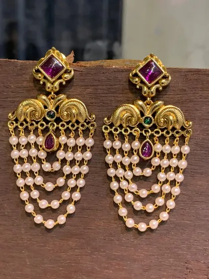 This version of the imitation pearl drop earrings features a rich ruby-colored stone. The design is inspired by traditional South Indian jewellery styles.