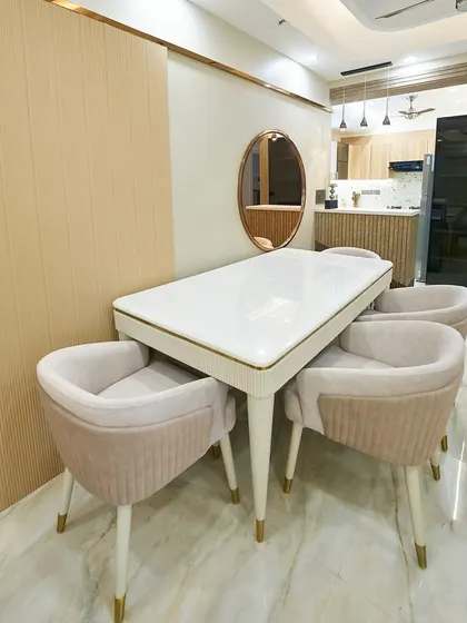 An elegant and cozy dining space with a white table and blush pink chairs. The fluted wall panel and oval mirror add modern, soft touches to the design.