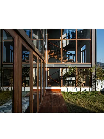 The exterior facade showcases the home's modern aesthetic, with clean lines and large glass panels. The reflection in the glass creates a beautiful symmetry with the surrounding greenery and the building's structure.
