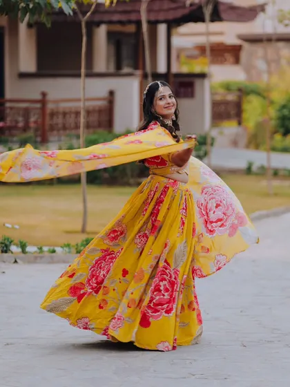 A joyful shot of the bride twirling in her vibrant yellow and pink floral lehenga, capturing movement and happiness.