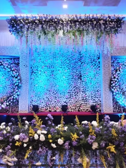 A modern reception stage featuring circular floral wreaths against a backdrop of white flowers and dramatic blue lighting, offering a contemporary yet elegant look.