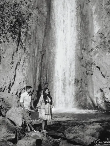 A classic black and white portrait by a waterfall. This wide shot captures the scale of the natural landscape while keeping the couple as the central focus of the story.