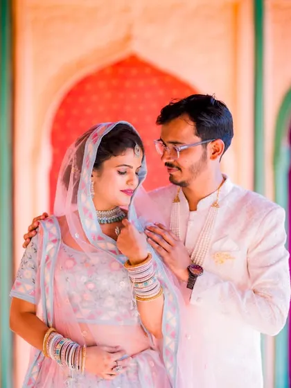 A tender moment between a couple, with the groom gently touching the bride's shoulder. Their elegant outfits and the vibrant background create a beautiful contrast.