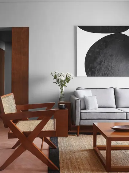 A living room scene with a custom grey sofa and a classic wooden armchair with cane details. I believe in mixing materials and styles to create a space that feels collected and personal.