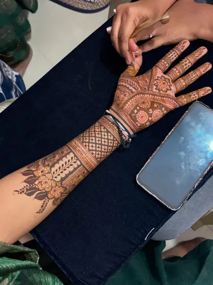 A close up of a detailed bridal mehendi application in progress. You can see the reference design on the phone, showing how I work with clients to bring their desired patterns to life with precision.