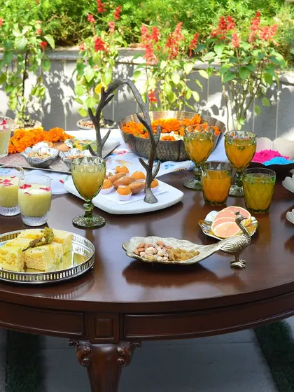 A full Holi party setup on our classic wooden table. The scene features our peacock platter, green glass goblets, and various trays, all ready for a celebration.