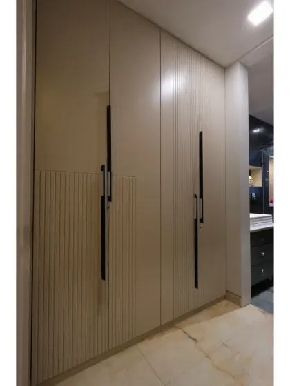 The adjacent wardrobe space features chic PU-finished wardrobes with long, modern handles and fluted detailing.