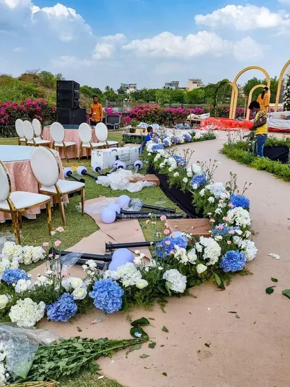 Here is a glimpse of the floral setup in progress for the lakeside ceremony. We are arranging beautiful blue and white hydrangeas along the aisle, bringing a touch of soft color to the grand outdoor space.