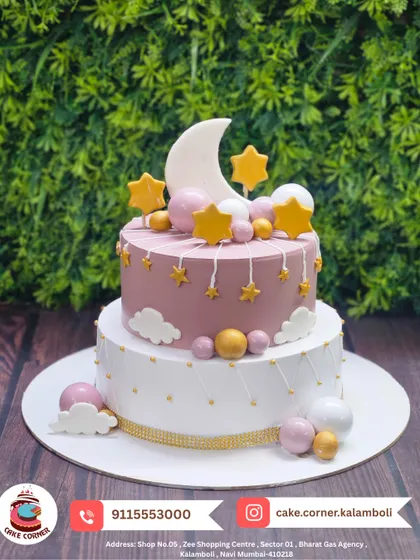 A dreamy two-tier cake with a moon and stars theme. The pastel pink and white colours, along with the golden stars, create a magical and serene look.