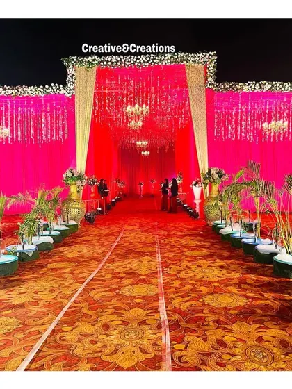 A grand outdoor entrance with pink draping and small fountains. The design combines vibrant colors with natural elements for a unique and festive look.