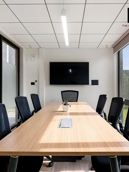 A bright and airy conference room with large windows offering views of the outdoors. The room is equipped with a large screen and a spacious table, designed for productive and comfortable meetings.