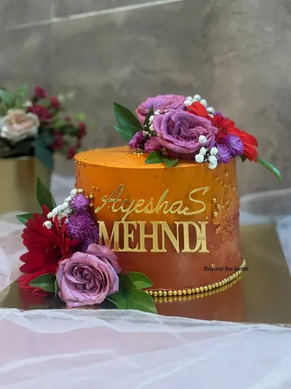 An orange ombre cake for a vibrant Mehendi celebration. The warm tones are complemented by fresh, colorful flowers, creating a stunning centerpiece for the bride to be.