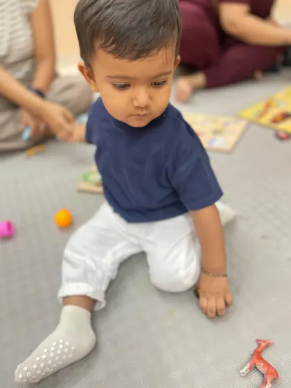 A toddler sits on the floor surrounded by toys, exploring them at his own pace during a free play session.