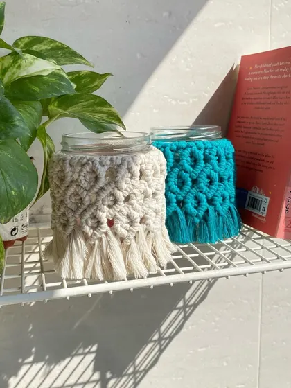Here are our macrame mason jars styled on a shelf with books and a plant. They add a perfect touch of handmade, boho charm.