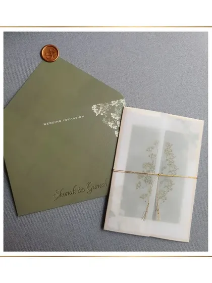 A close-up of the olive green invitation suite, showing the vellum wrap tied with twine and secured with a wax seal. This layering adds a touch of rustic charm to the elegant design.