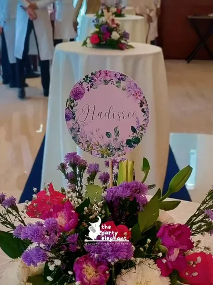 A beautiful floral centerpiece with a personalized "Nadiree" sign. We create custom table decor that incorporates the event's theme and color palette for a cohesive look.
